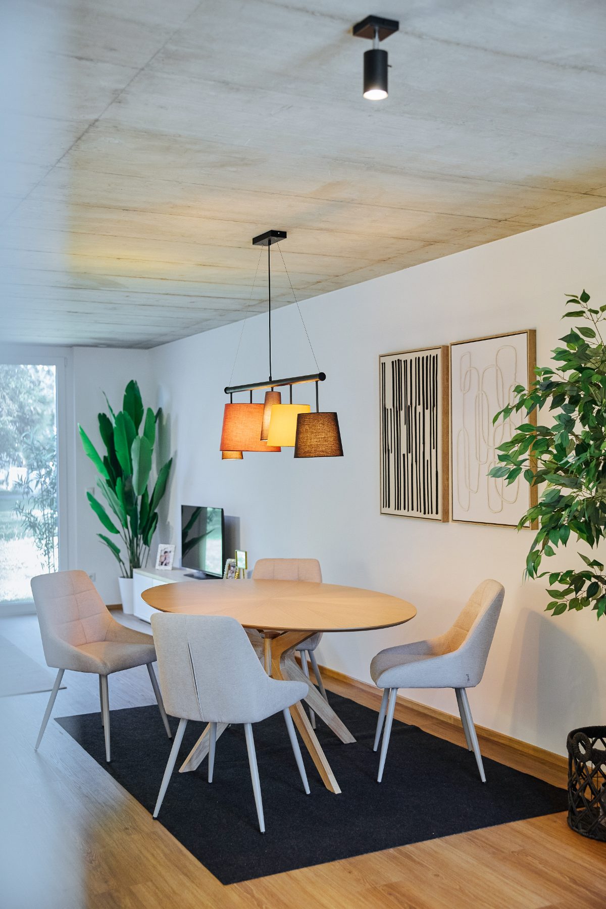 Essbereich mit rundem Holztisch, hellen Stühlen und Pendelleuchte unter einer Sichtbetondecke